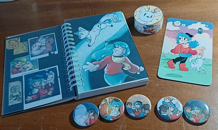 Notebook opened beside buttons, washi tape and a standee.